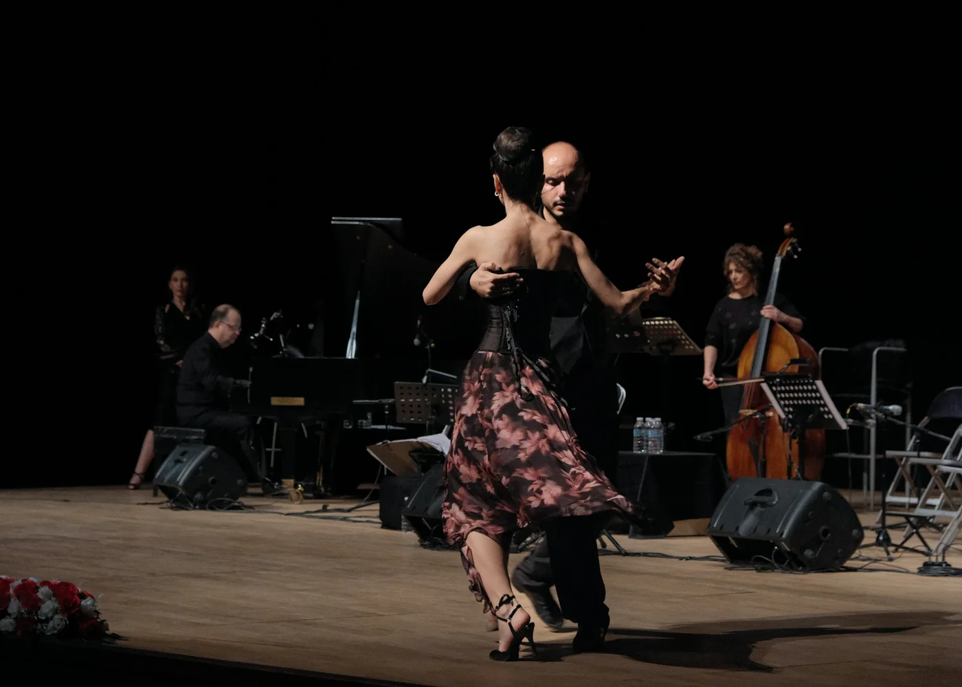 Et tangopar, der danser på scenen foran et liveorkester med klaver og kontrabas, repræsentativt for Tango Porteños live-musikproduktion